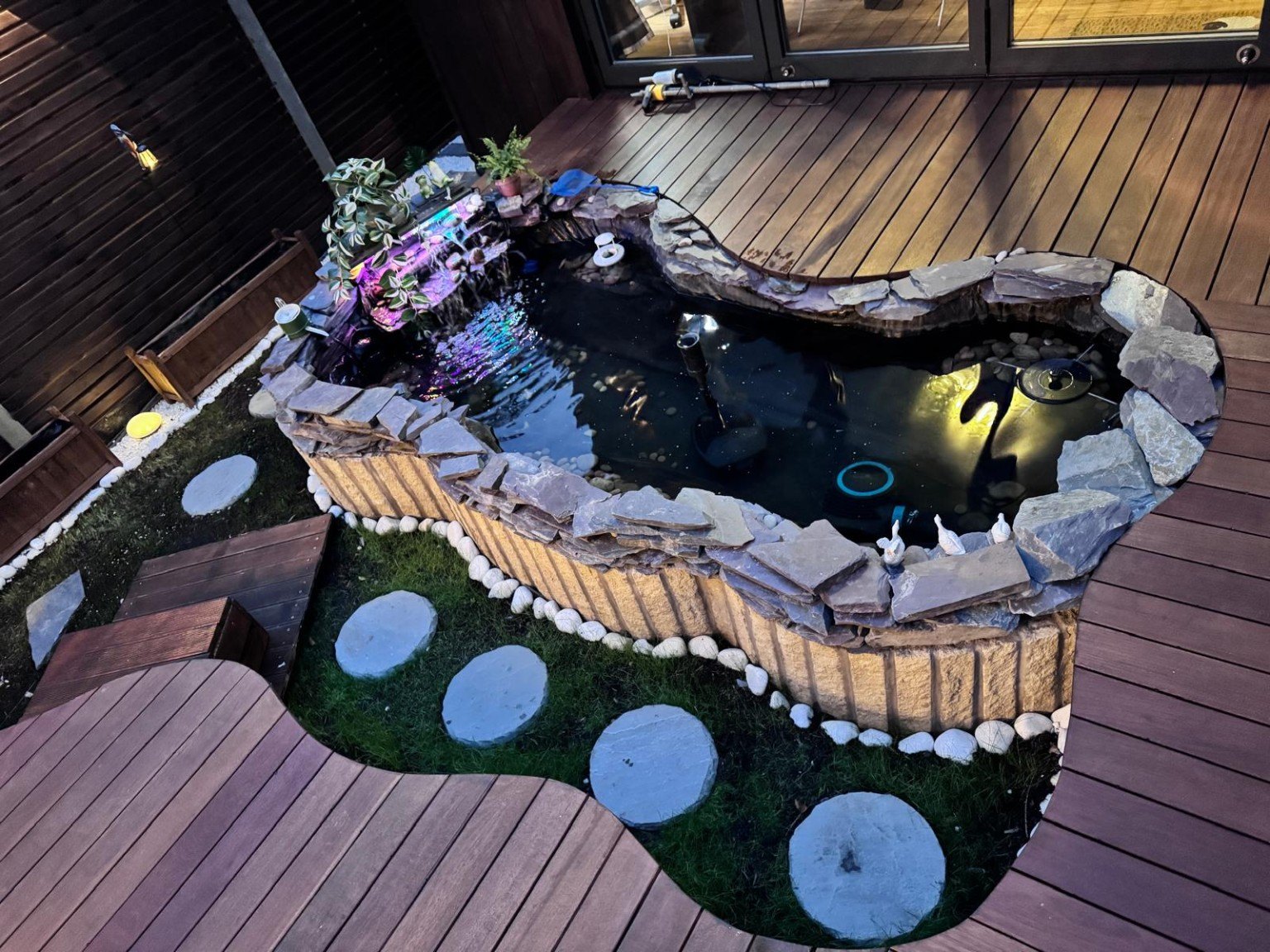 Completed garden pond framed by timber decking and stepping stones